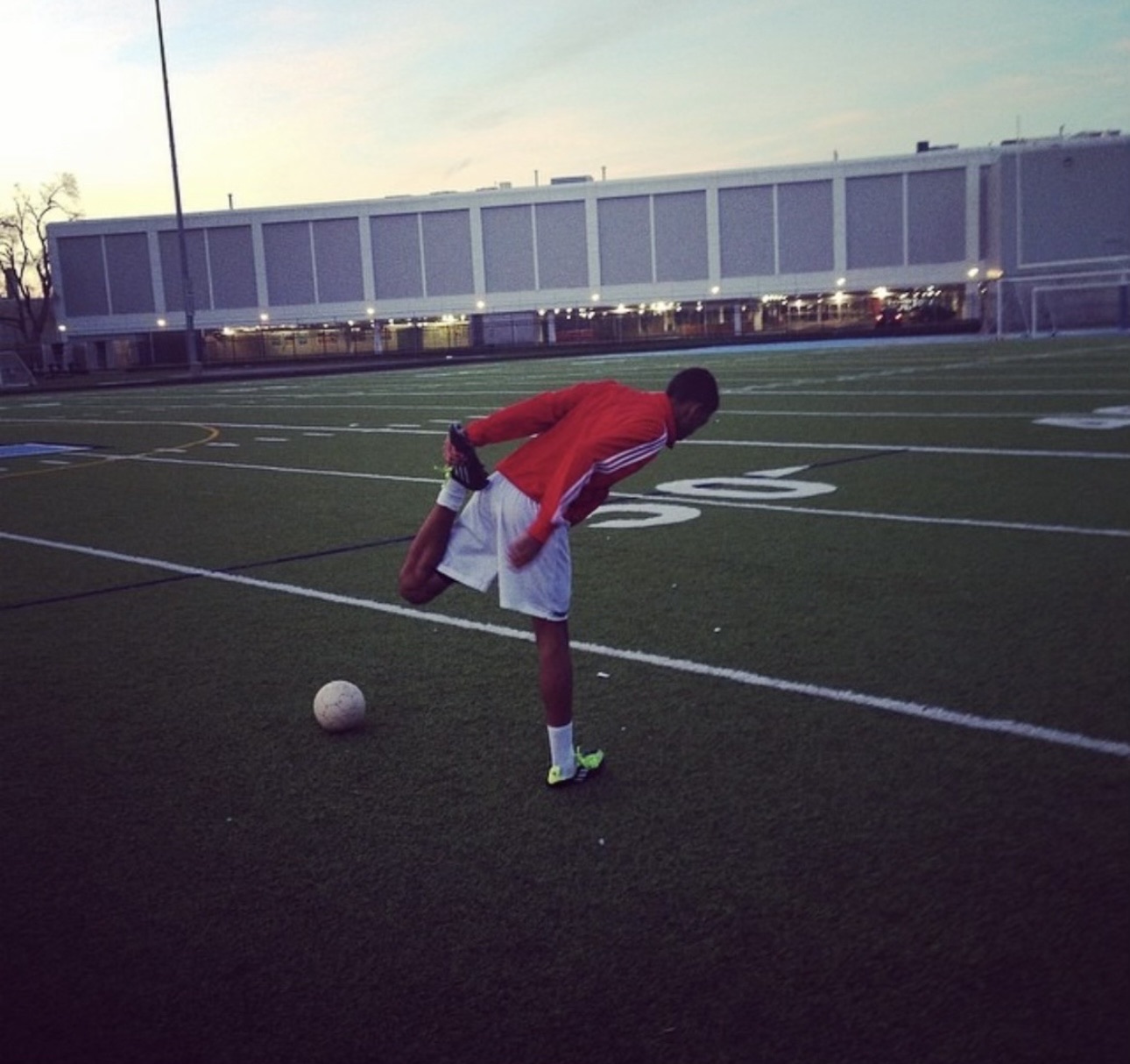 The Pathwai founder stretching alone on a turf field at dusk, a ball at his feet